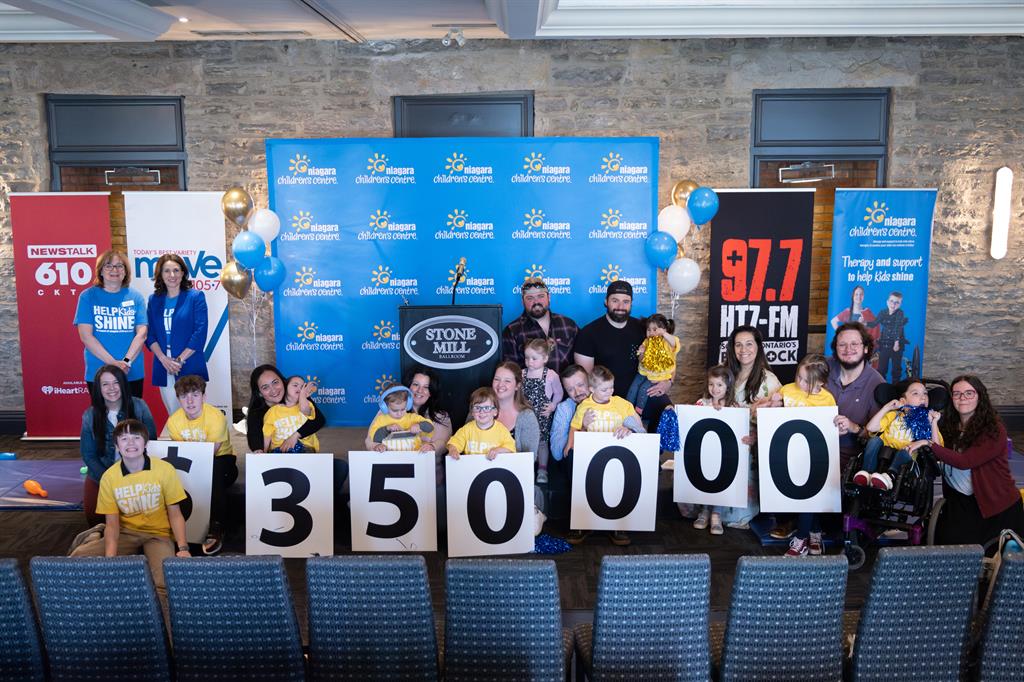Families sitting in a row holding white number signs reading $350,000